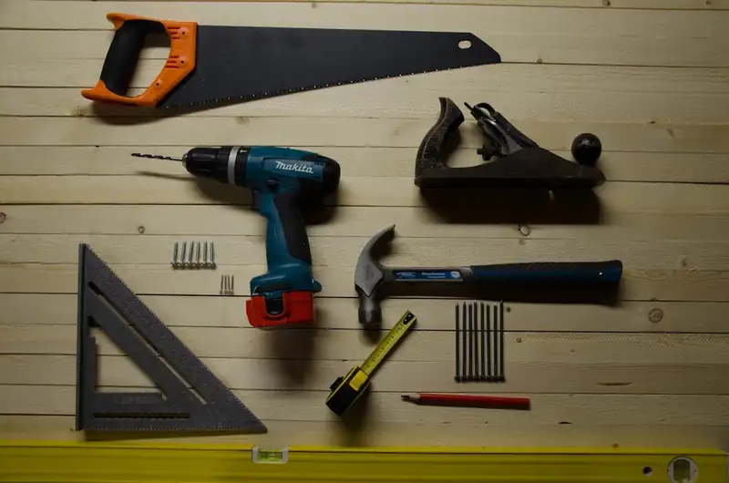 Assorted hand tools laid out deliberately on a wooden surface, including a saw, drill, plane, and tape measure
